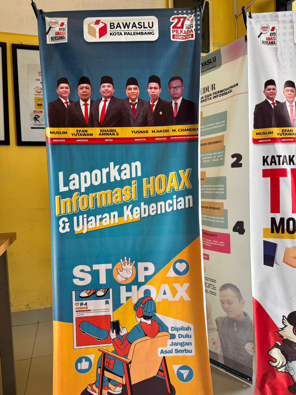 Spanduk kampanye Stop Hoaks terpajang di area Sekretariat Bawaslu Kota Palembang, menampilkan jajaran pimpinan Bawaslu Kota Palembang (dari kiri ke kanan): Muslim, Efan Yutawan, Khairil Anwar S., Yusnar, M. Hasbi, dan M. Chandra, Selasa (4/11/2025). Foto: Tim Humas Bawaslu Kota Palembang